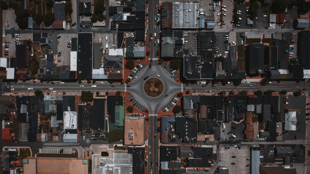 Overhead view of circle roadway near parking and driving vehicles between house roofs in town