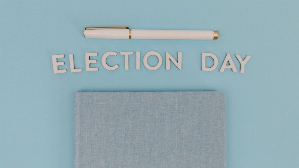 Blue notebook and pen against a light blue background reading 'Election Day', ideal for campaign themes.