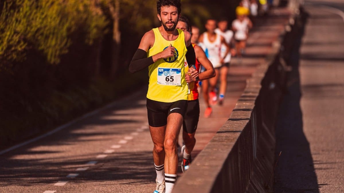 Focused male athlete running in a marathon on a sunlit road, leading a group of runners.