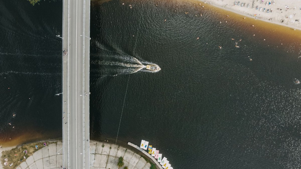 A boat speeding under a bridge on a river in Kyiv, capturing summer vibes.