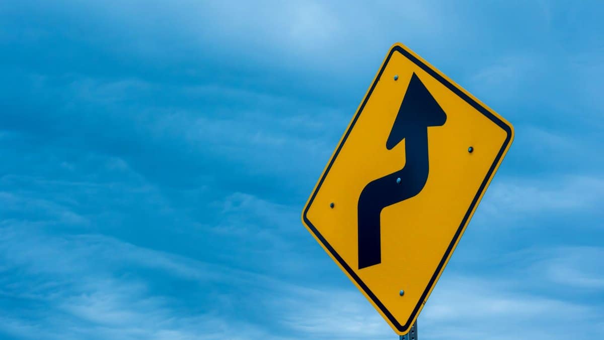 Yellow right turn road sign with blue sky background, symbolizing traffic and safety.