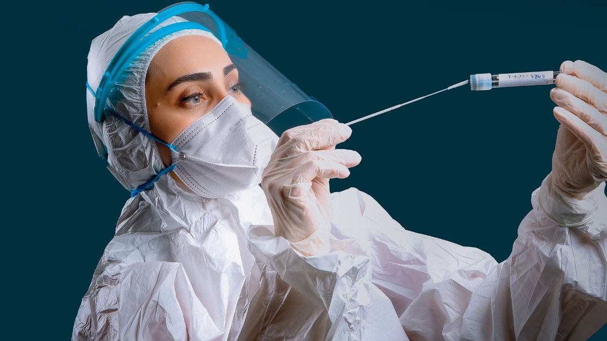 A healthcare worker in full PPE holding a test swab, representing health safety and virus testing.