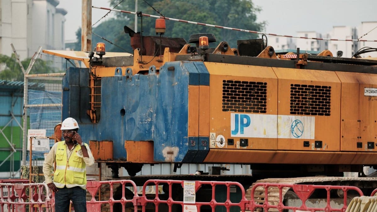 Worker on phone at construction site with large machinery in urban setting.