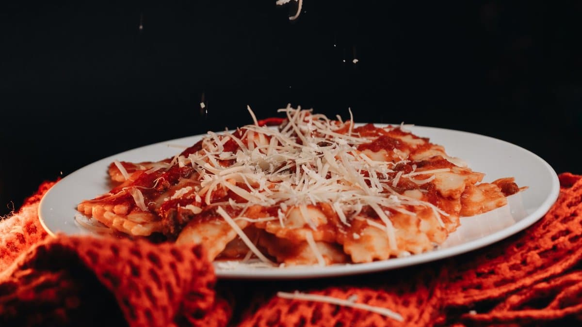 Close-up of ravioli topped with tomato sauce and grated cheese on a plate.