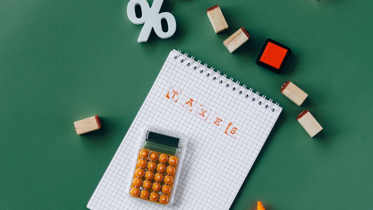 Flat lay of tax essentials with calculator, notebook, and stamps on a green background.