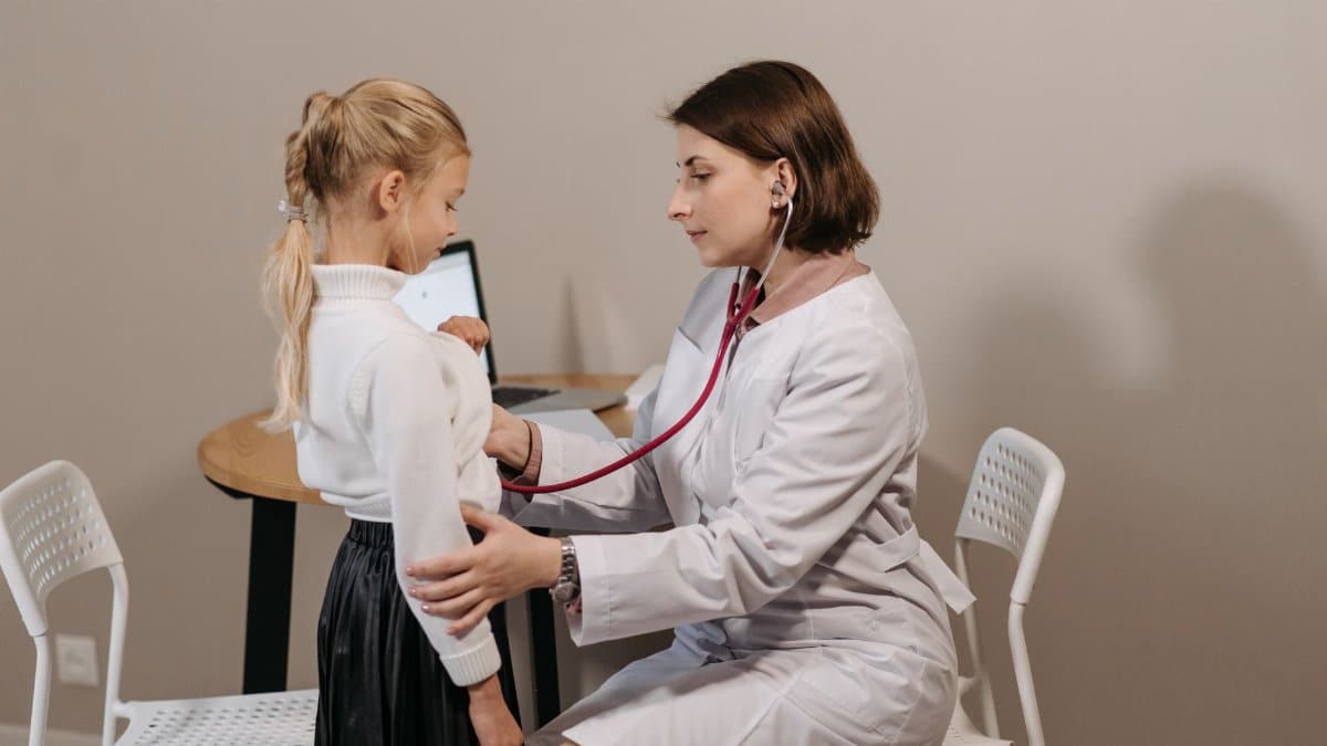 A pediatrician listens to a child's heartbeat during a check-up in a clinic setting.