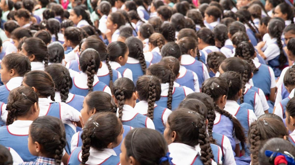 A gathering of schoolgirls in uniforms with neatly braided hair, viewed from behind.