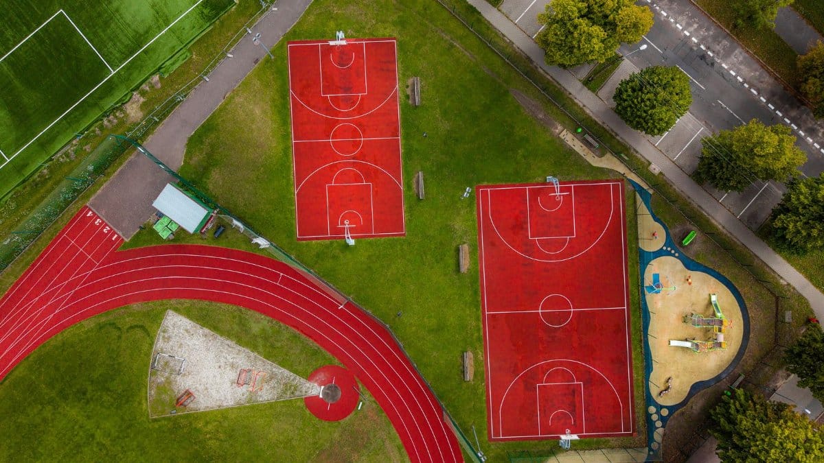 Aerial view of a sports complex with red basketball courts, a football field, and a running track.