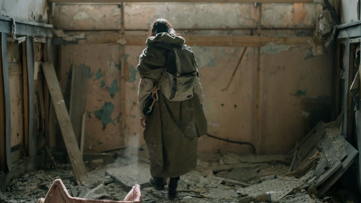 A lone figure explores an abandoned building, covered in debris and decay.