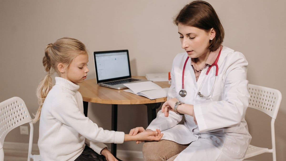 A doctor examines a young girl during a pediatric consultation in an indoor clinic setting.