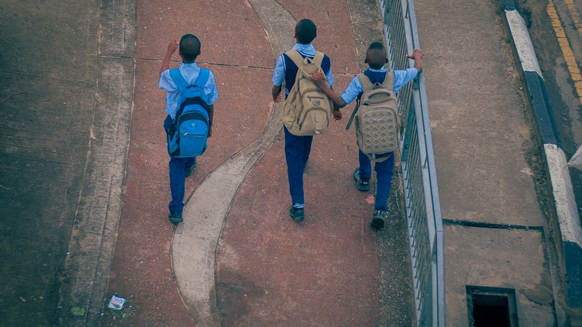 Three teenage schoolboys walk on a paved path in Uyo, Nigeria, viewed from above.