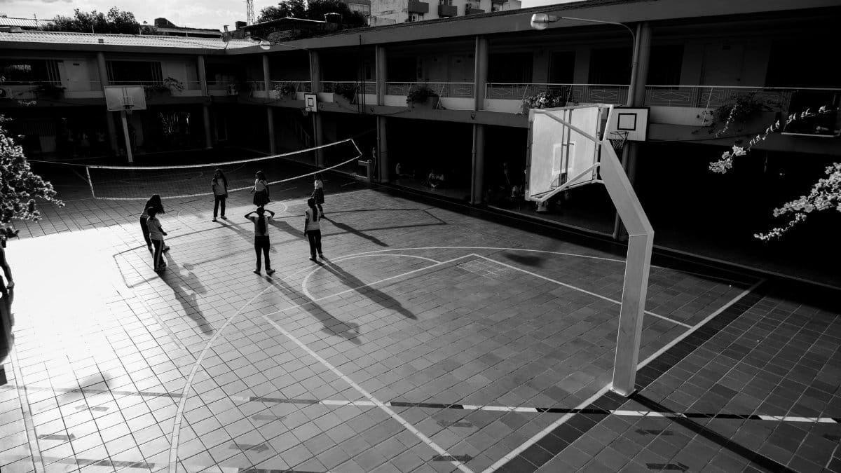 Black and white image of a basketball court with players casting long shadows at sunset.