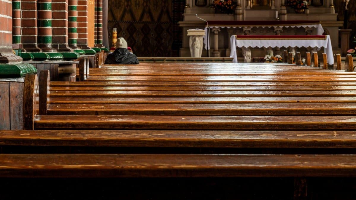 Empty church interior with wooden pews leading to richly decorated altar, warm atmosphere.