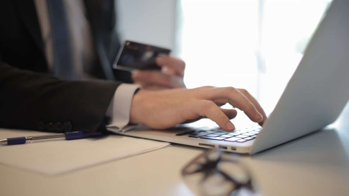 Man in suit using laptop and credit card for online transaction at work.