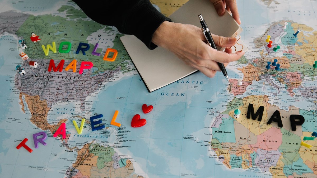 Hands holding pen and notebook over vibrant world map planning a journey.