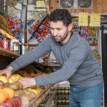 Grocery store worker organizing fresh fruits and vegetables on display shelves.