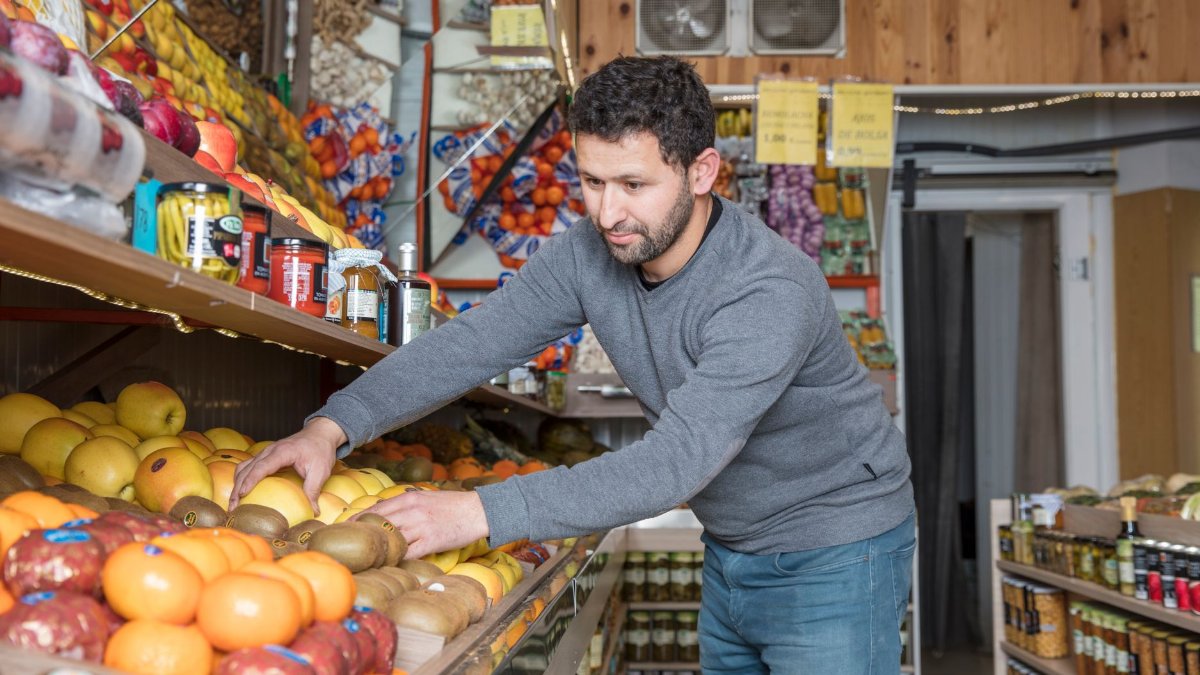 Grocery store worker organizing fresh fruits and vegetables on display shelves.