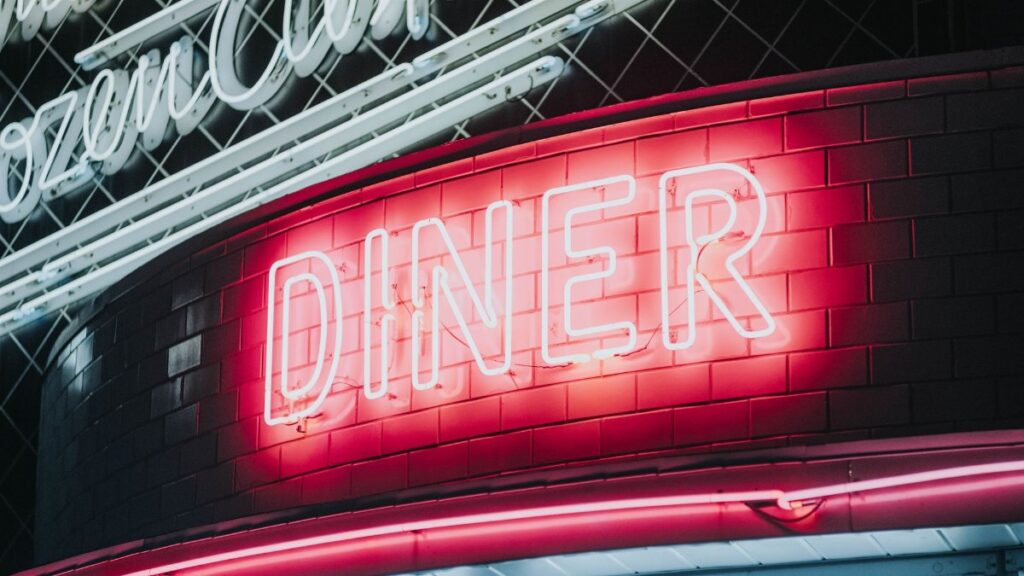 Bright neon diner sign glowing against dark tiled wall, evoking a vintage retro vibe.