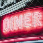 Bright neon diner sign glowing against dark tiled wall, evoking a vintage retro vibe.