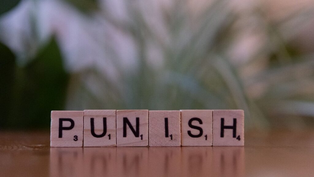 Scrabble tiles spelling 'punish' against a blurred natural background.