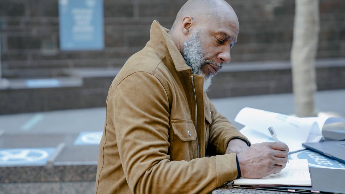 Mature businessman writing notes outdoors in a city setting, highlighting urban lifestyle and work.