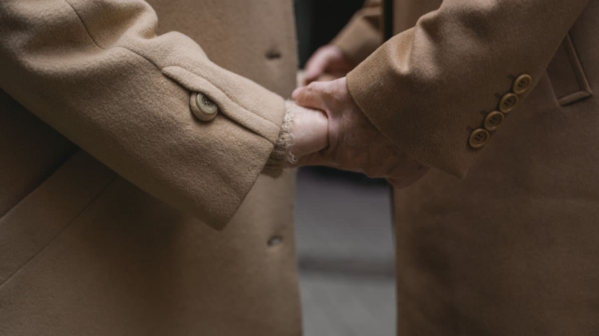 Two people holding hands in friendship or affection, wearing brown coats.