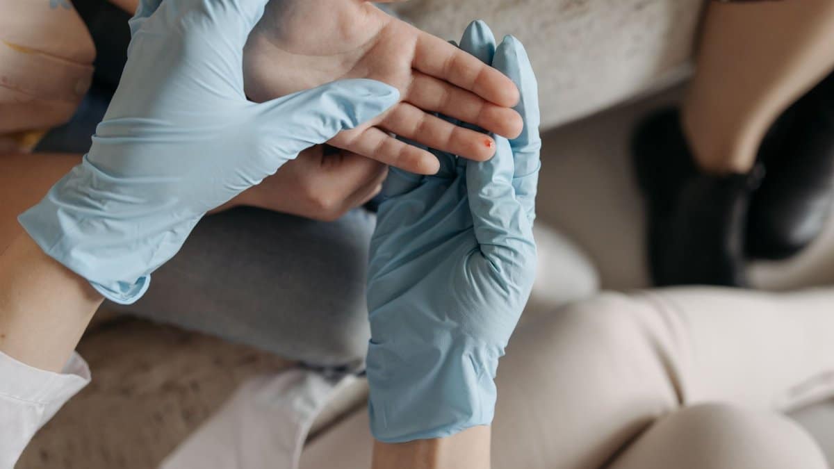 A medical professional wearing blue gloves examines a small wound on a person's finger indoors.