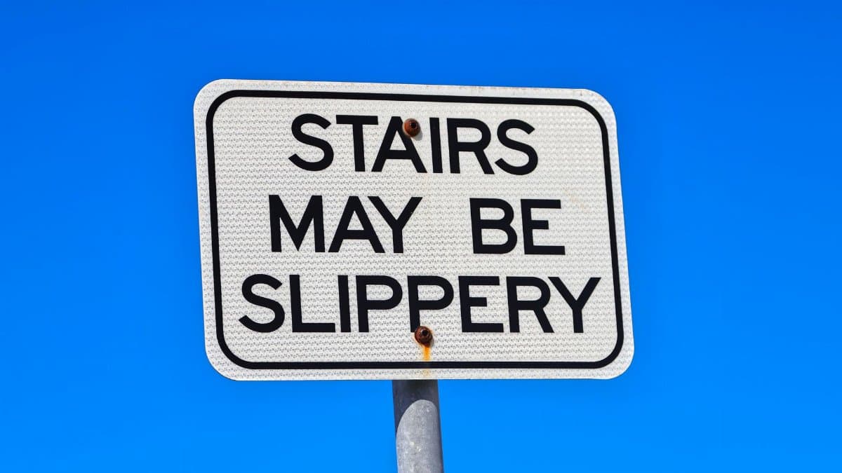 Close-up of a warning sign reading 'STAIRS MAY BE SLIPPERY' against a clear blue sky.