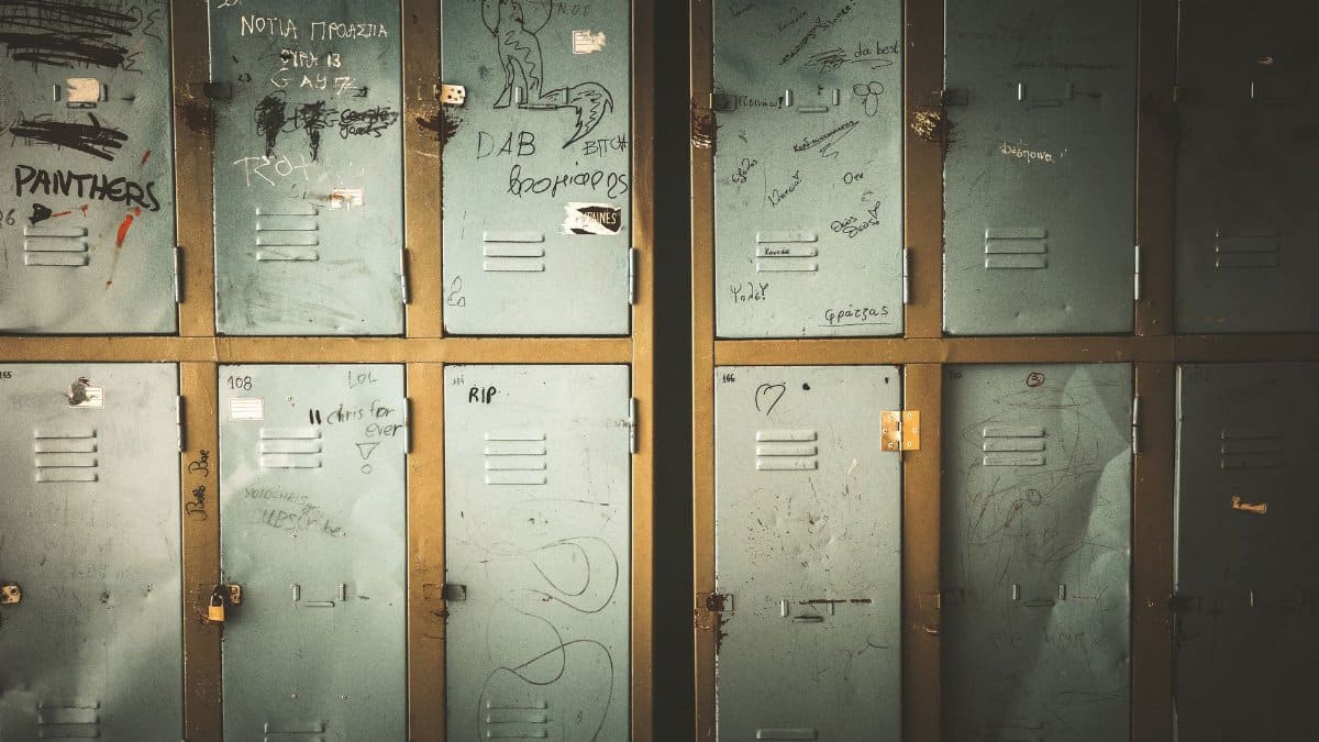 A row of old metal lockers with graffiti, showcasing urban decay and neglect in a dimly lit locker room.