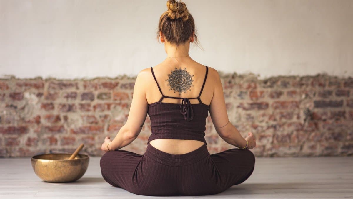 Woman meditating indoors with a tattoo on her back, embracing peace and zen.