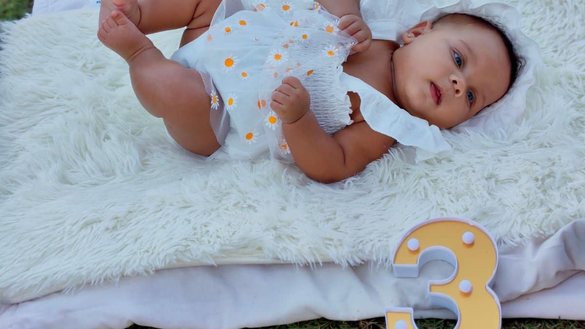 A cute baby lying on a fluffy blanket, marking three months old with a decorative number three sign.