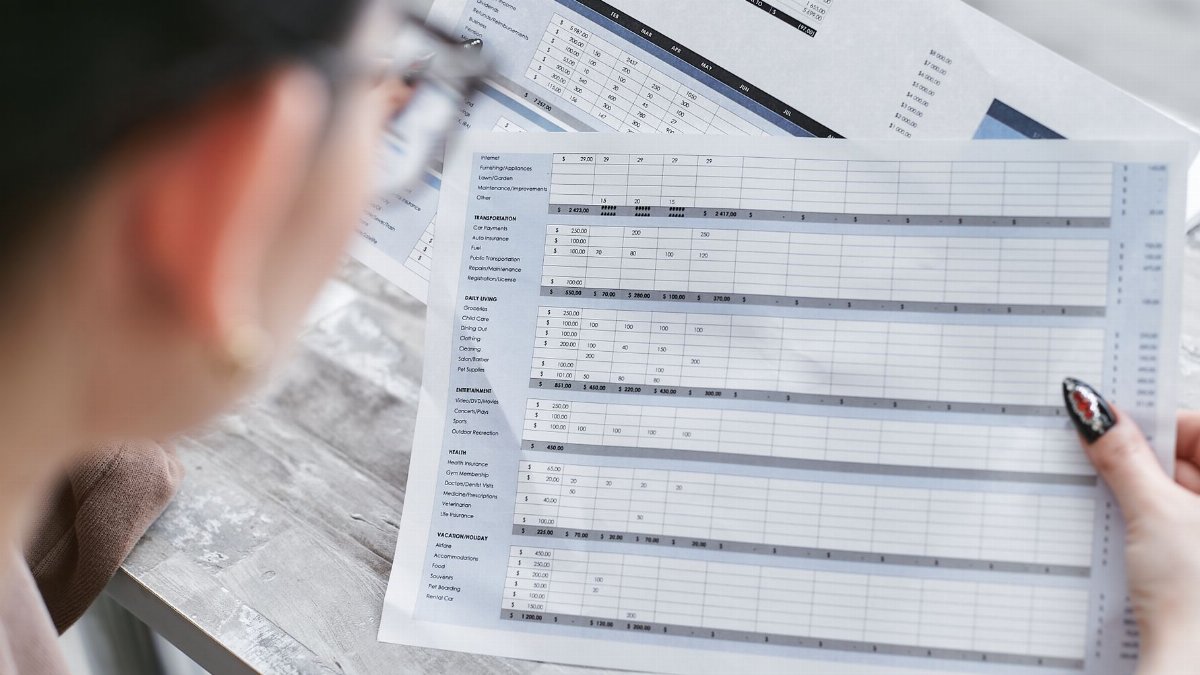 A businesswoman reviewing financial spreadsheets with charts and graphs in an office setting.