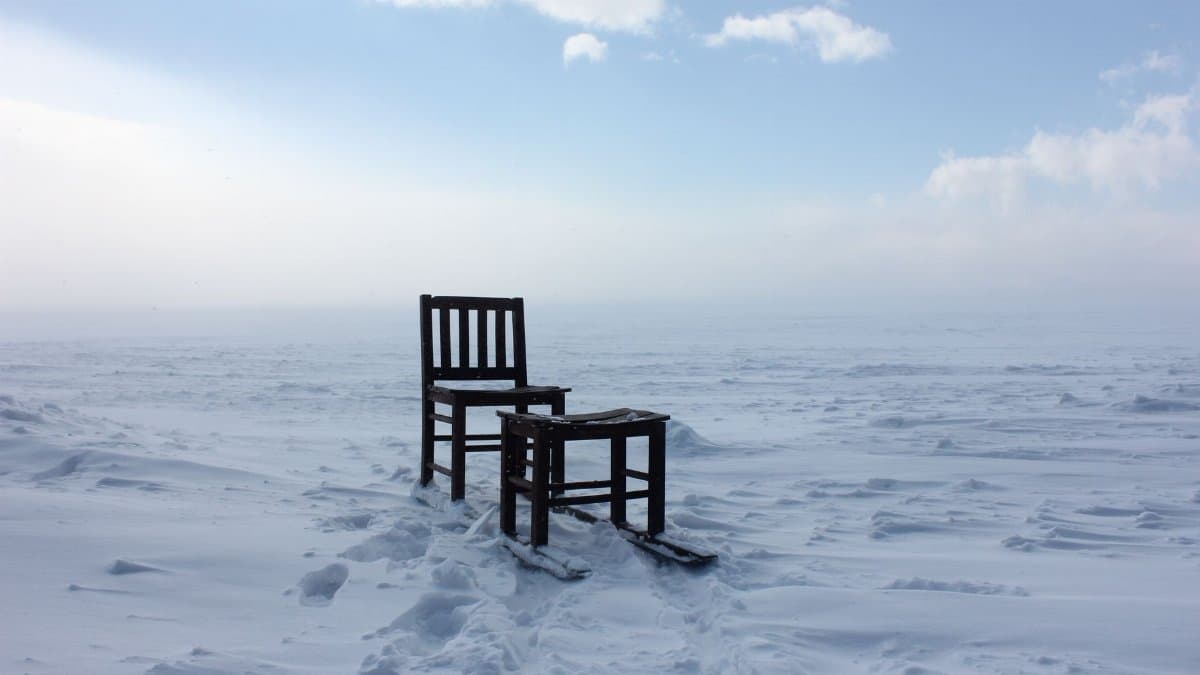Solitary wooden chair amidst a vast, snow-covered winter landscape.