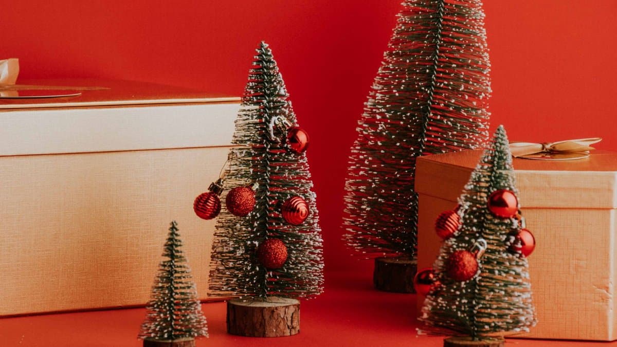 Small decorated Christmas trees with gifts against a red background.