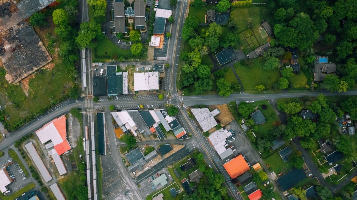 Drone view outpost town district with contemporary cottages and large industrial buildings surrounded with lush tree on summer day