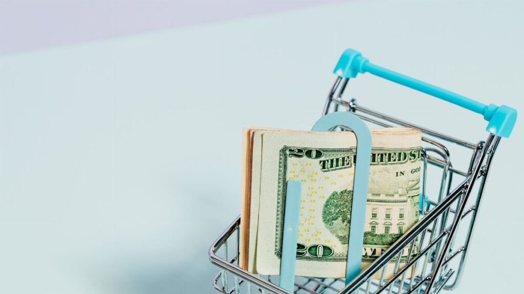 A shopping cart holding a stack of US dollar bills symbolizes financial savings and consumer spending.