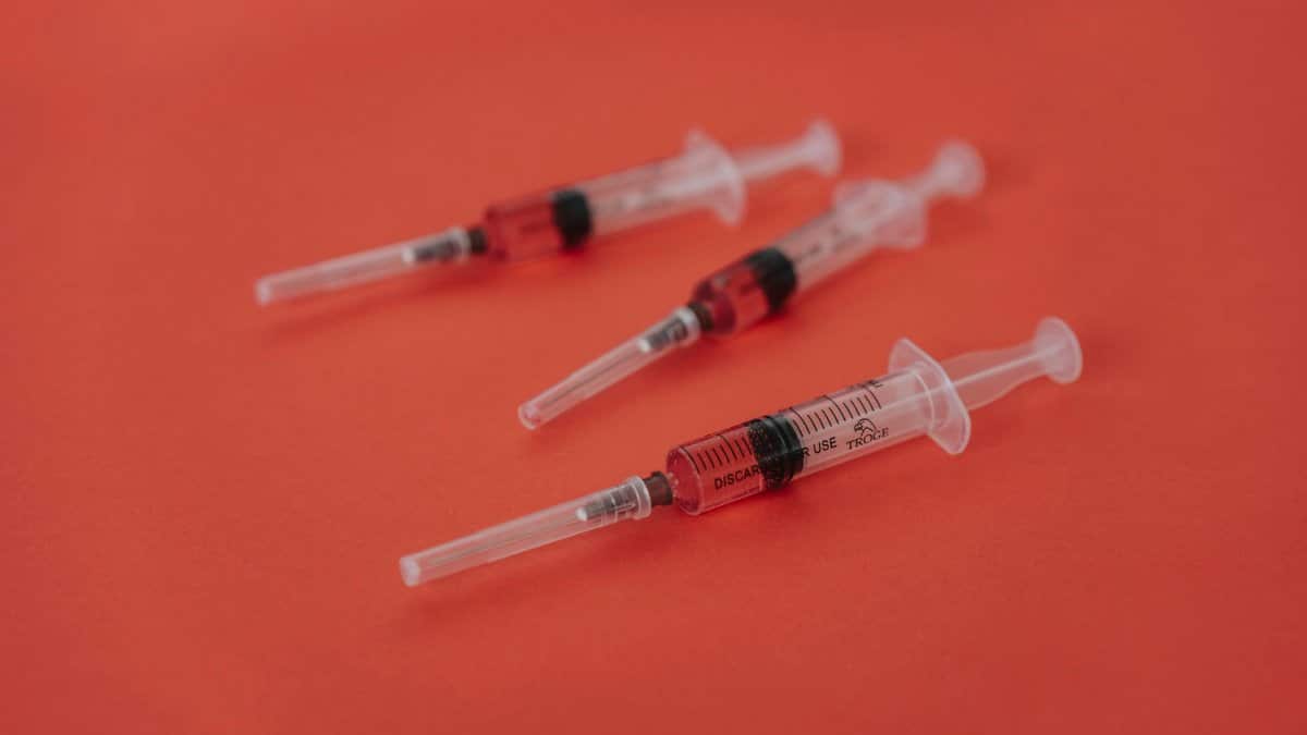 Three syringes with red liquid on a bold red surface, featuring medical themes.