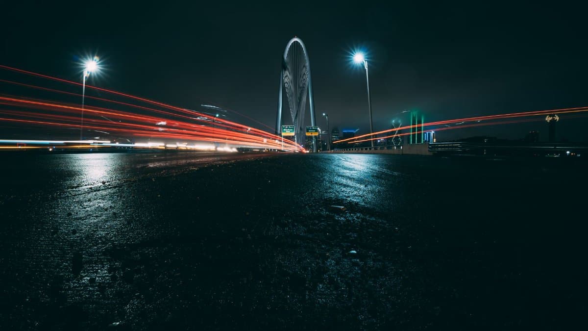 Dramatic long-exposure of Dallas bridge with car lights streaking under a night sky.