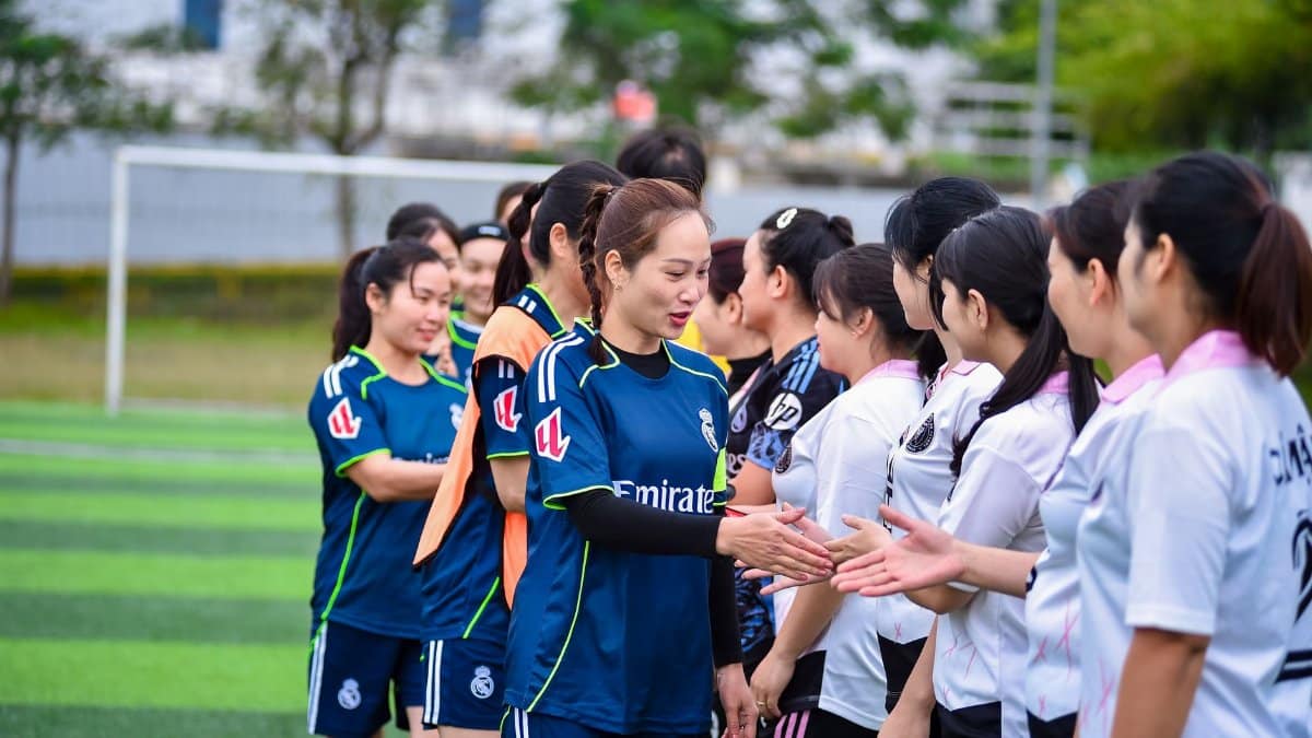 Women's football teams exchanging handshakes on a sports field in Hà Nội, Vietnam.