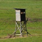 Wooden hunting stand overlooking a vast green field, ideal for wildlife observation.