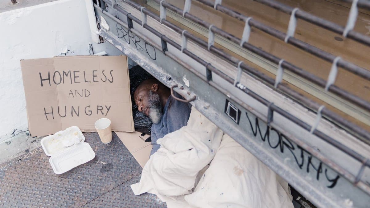 A powerful depiction of a homeless man sleeping with a sign reading 'Homeless and Hungry.'