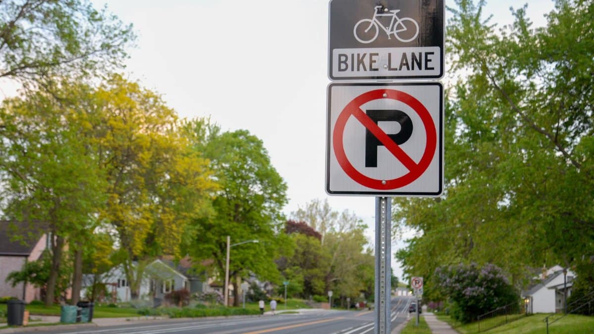 Suburban road with a bike lane and no parking sign, bordered by trees.