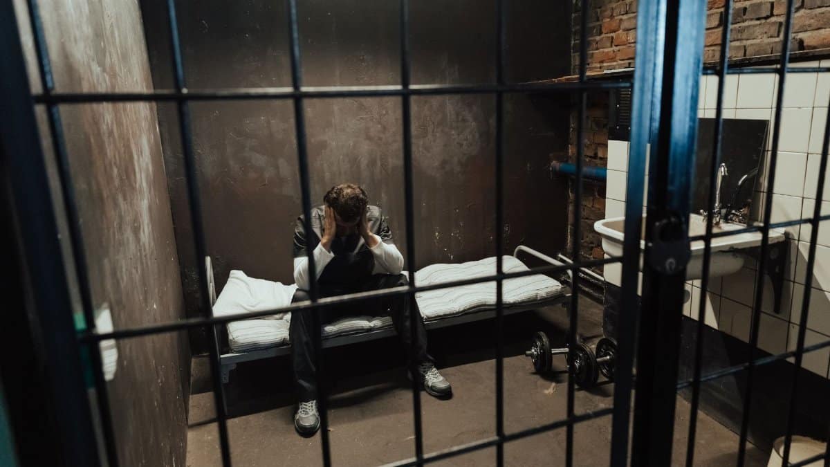 A man sits in a jail cell, reflecting on his thoughts, emphasizing isolation.