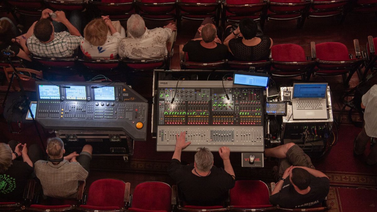 Top view of sound engineering equipment in use during a theater performance, with operators seated.