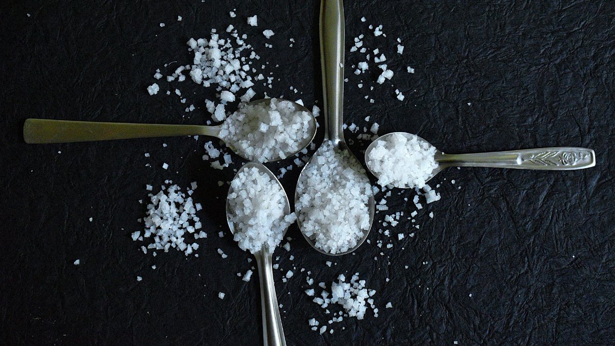 Overhead view of coarse sea salt on silver spoons against a textured black background.