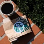 A coffee cup and Starbucks bag on a sunny brick surface in Poznań, Poland.