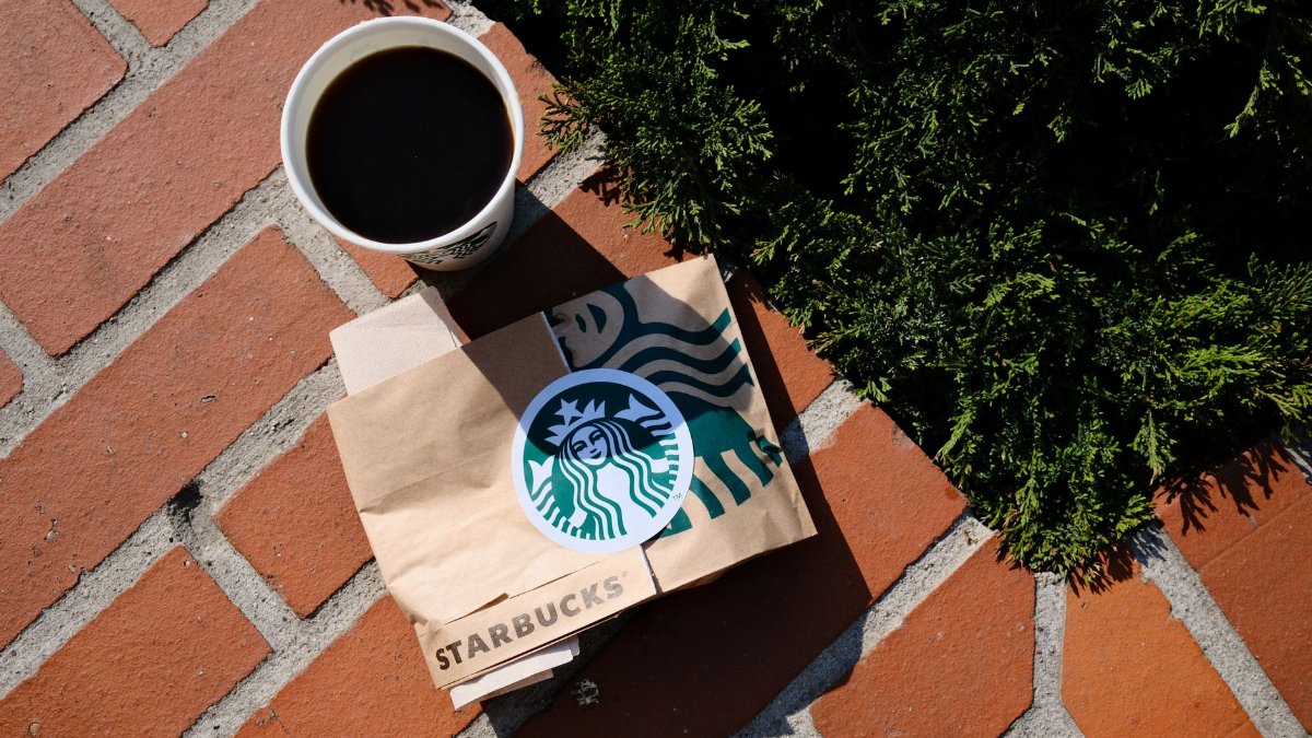 A coffee cup and Starbucks bag on a sunny brick surface in Poznań, Poland.