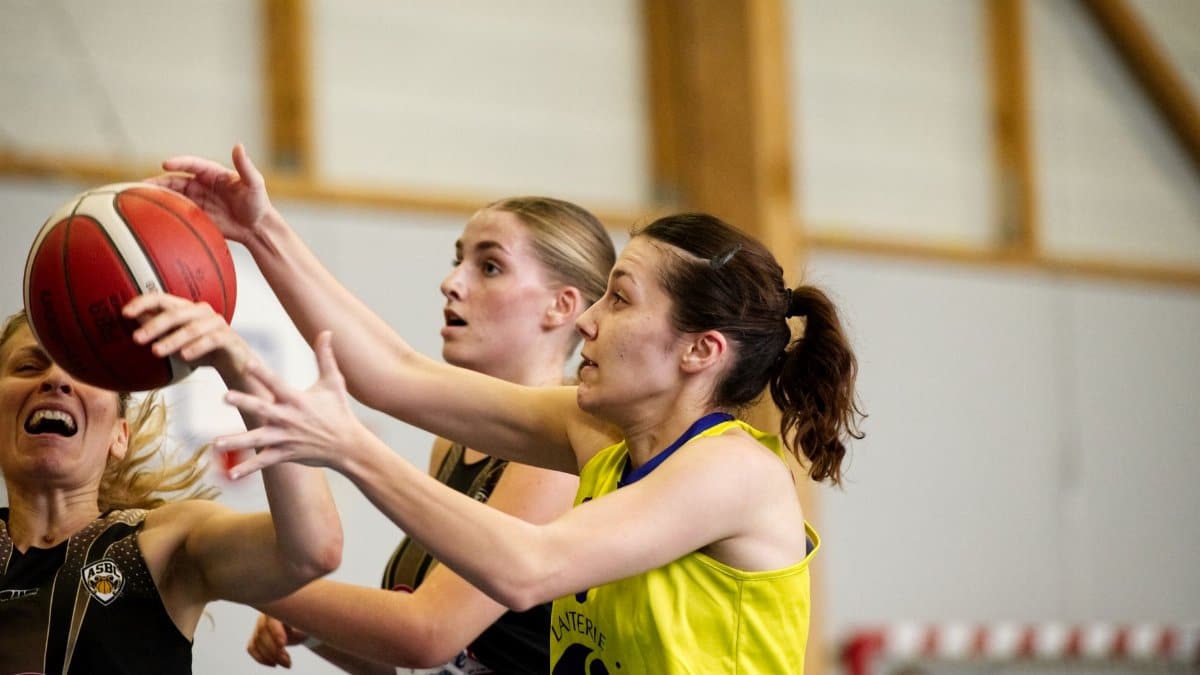 Close-up of women basketball players in a competitive game, reaching for a ball indoors.