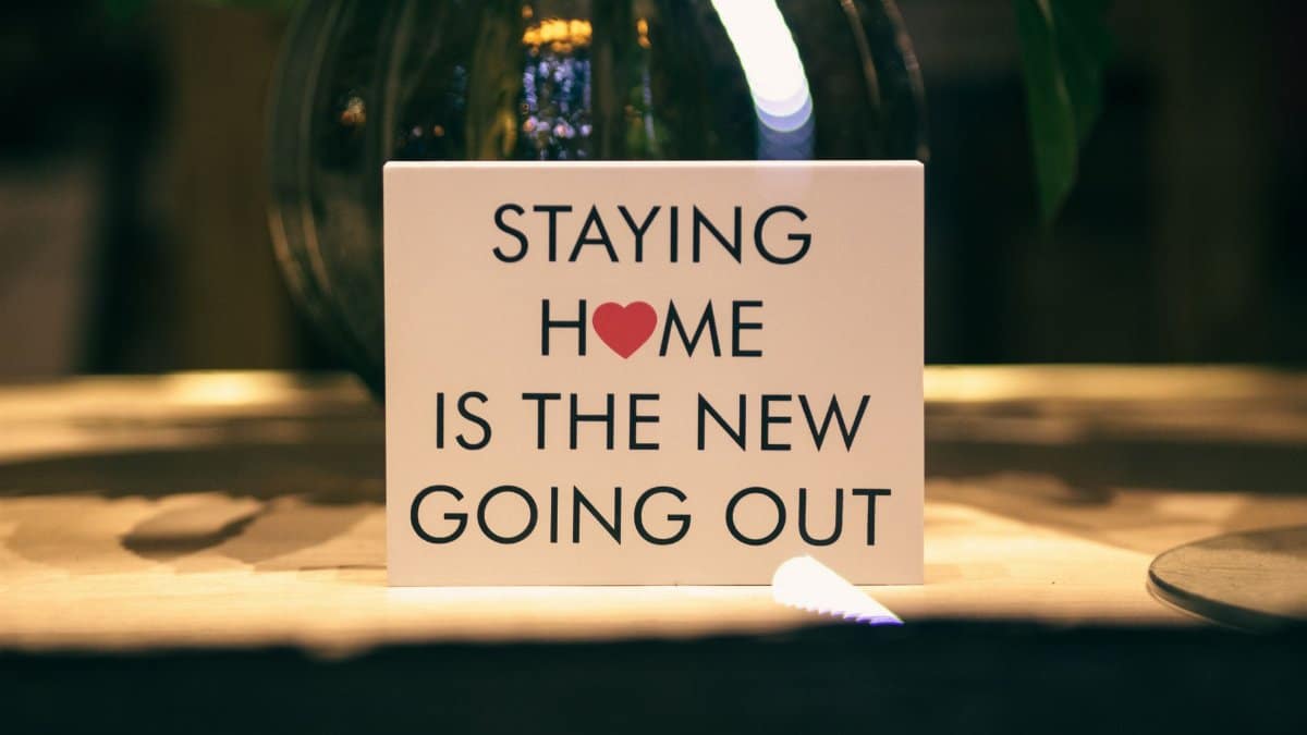 A decorative sign reads 'Staying Home is the New Going Out' indoors with warm ambiance.
