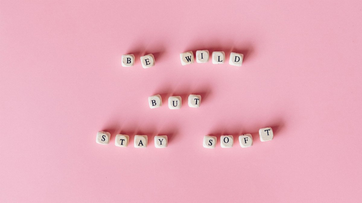 Scrabble tiles spelling 'Be Wild but Stay Soft' on a pink background.